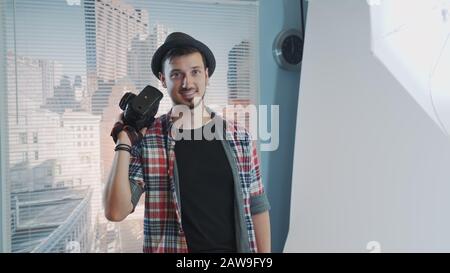 Smiling young photographer posing with his professional camera. There are skyscrapers in the background. Stock Photo
