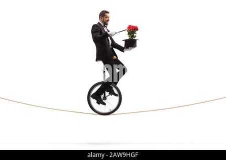 Magician with a wand riding a unicycle and performing a trick with red roses and a hat isolated on white background Stock Photo