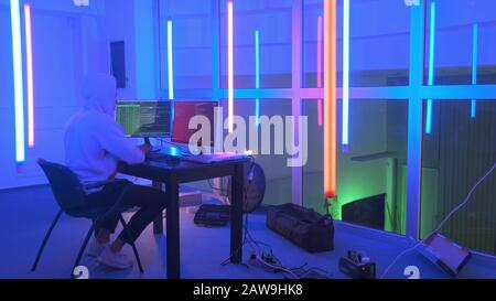 Hacker working place: hacker working in a room with colored neon lights. He writing hacker program. Stock Photo
