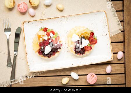 Fruit tarts and macaroons on a wooden background with folk and knife. Top view, horizontal, warm color Stock Photo