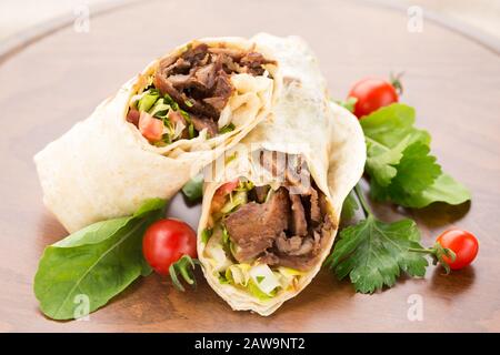 Doner kebab with cherry tomatoes and salad on wooden background. Natural light, horizontal Stock Photo