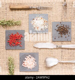 Spices on dark plates with rosemary, antique forks, spoon and knife. Salt and pepper. Rustic background. Warm color. Square Stock Photo