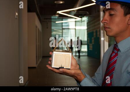 Architect holding mock-up of house with the key inside that they will deliver to their clients along with the work team to provide user experience in Stock Photo