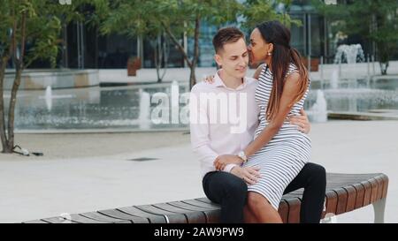 Young mixed-race family having nice time outdoors: laughing, hugging and talking to each other. The fountains are in the background. Stock Photo