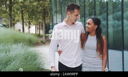 Tall young man kissing her african girlfriend while walking down the street. She telling him about something. Relationship concept Stock Photo