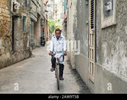 Diu, India - December 2018: A man rides a bicycle through a narrow lane in the town of Diu. Stock Photo