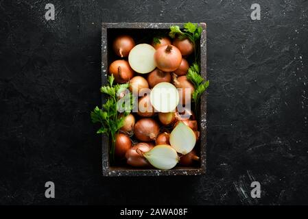 Fresh ripe onions in wooden box on black background. Top view. Free copy space. Stock Photo