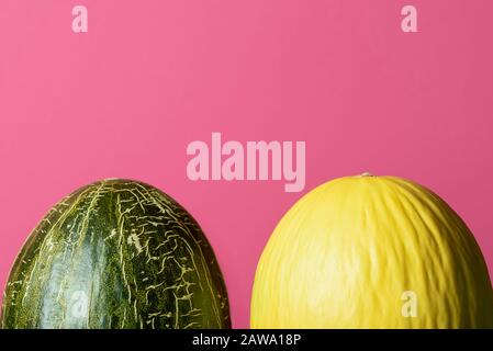 Two sweet melons on pink background. Green and yellow melons. Fresh summer fruits. Honeydew melon and frog skin melon isolated on a red background. Stock Photo