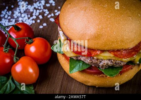 Craft beef burger with cheese, italian peperoni, tomato and basil leafs on wood table and rustic background Stock Photo