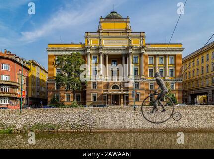 Old style cyclist sculpture (designed by Enes Sivac in 1993) hanging over the Miljacka river, with the University Faculty of Law in the background Stock Photo
