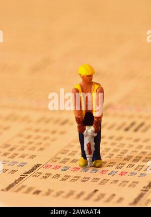 Model of man with pneumatic drill and wearing hard hat, standing on stocks and shares page of financial newspaper. Stock Photo