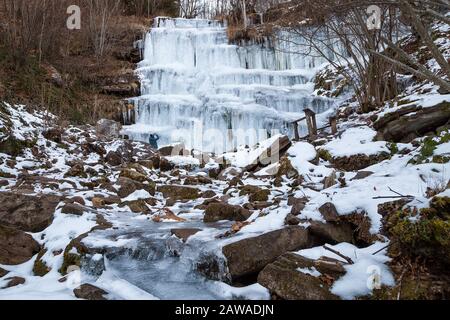 Mountain hiker photographing beautiful, scenic, frozen Tupavica waterfall with hanging icicles and frozen mountain creek with orange rocks Stock Photo
