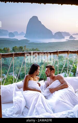 couple waking up in bed in nature jungle looking out over ocean during sunrise at wooden hut in the moutains of Thailand Stock Photo