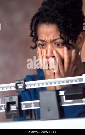 An African-American woman is shocked looking at her weight on a doctor scale after dieting Stock Photo