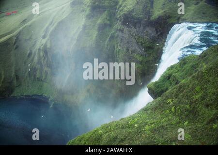 dramatic view of birds flying over Skogafoss waterfall in Iceland on overcast day Stock Photo