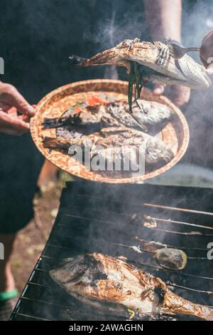 A man holds a plate with a ready meal. delicious and fresh grilled fish with lemon on the Barbeque grill at the garden in summer. Selective focus Stock Photo
