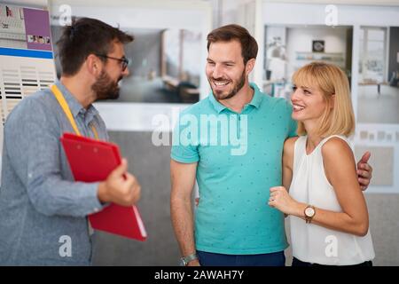 designer showing sketches and catalogue of products for interior decor to a young couple at store Stock Photo