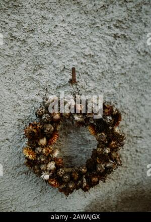 Stylish dried flowers wreath hanging from rusty hook on uneven wall Stock Photo