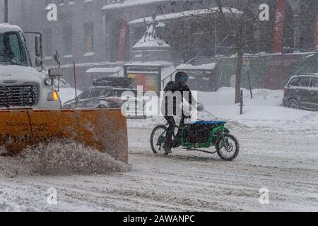 Montreal, CA, 7 February 2020: Man riding bike in Downtown Montreal during snow storm Stock Photo