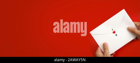 Valentine's Day background. A hand with white envelope and red heart on red background. Valentines day concept. Flat lay, top view, copy space Stock Photo