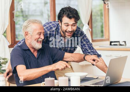 old man fun smile happy to looking at laptop with son. using communication technology for family happiness elder home care to connection other concept Stock Photo