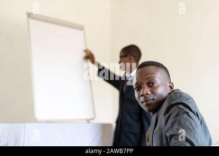 Public looking at camera while African CEO presents something on a White Board Stock Photo