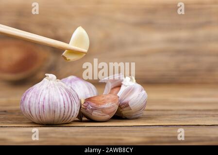 Several heads of garlic on a wooden background. Wooden chopsticks with a clove of garlic. Rustic stile. Copy space. Stock Photo