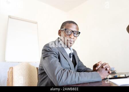 Authentic African black businessman in suit, glasses and tie posing for the camera in his office with office background Stock Photo