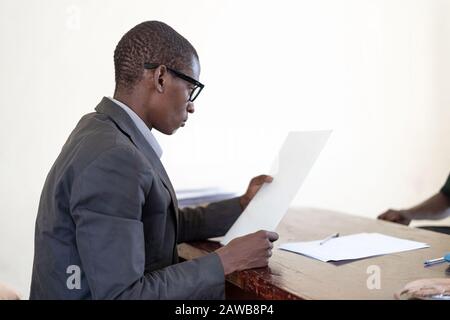 African businessman reading CV of student job application applicant during interview in office in Bamako, Mali Stock Photo