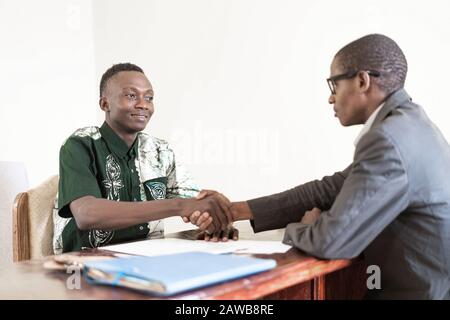 Two African business men smile and look at each other after sealing a deal together with shirts and suit and glasses in office in Bamako, Mali Stock Photo