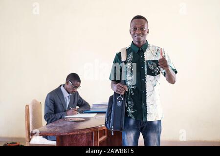 African young male student holding up thumbs up fingers and hands as a symbol for success in African studio in an African capital Stock Photo