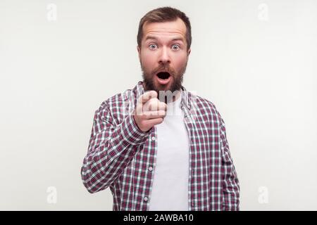 Hey you! Portrait of astonished bearded man in plaid shirt pointing finger at camera, standing with his mouth open and surprised shocked expression on Stock Photo