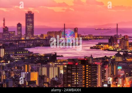 Red colourful sunset in Osaka city over sea horizon from the top of skydeck skyscraper tower towards sea port terminal and ships. Stock Photo