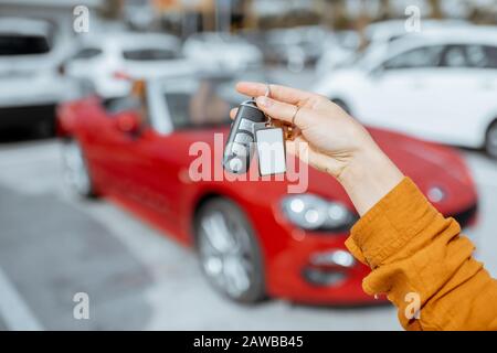 Woman holding keychain of a new purchased or leased red car at the parking place outdoors, close-up on hands and keys Stock Photo