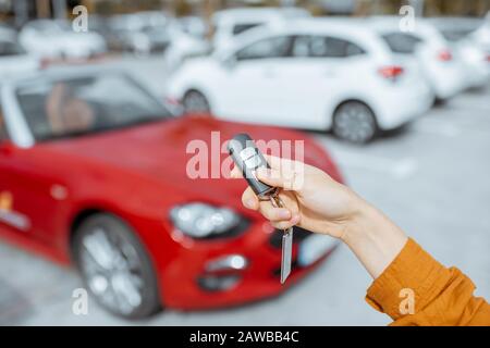 Woman holding keychain of a new purchased or leased red car at the parking place outdoors, close-up on hands and keys Stock Photo