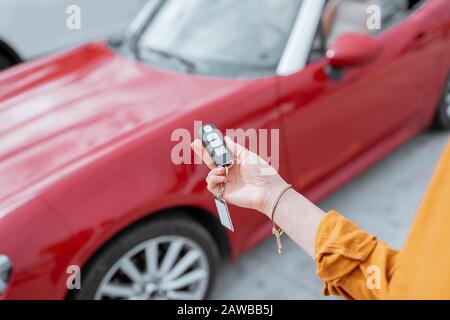 Woman holding keychain of a new purchased or leased red car at the parking place outdoors, close-up on hands and keys Stock Photo