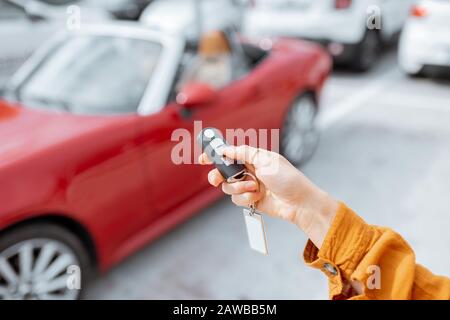 Woman holding keychain of a new purchased or leased red car at the parking place outdoors, close-up on hands and keys Stock Photo