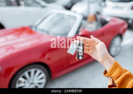 Woman holding keychain of a new purchased or leased red car at the parking place outdoors, close-up on hands and keys Stock Photo