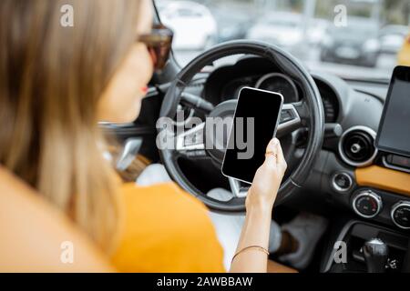 Young woman using smart phone while driving car, smart phone with black screen to copy paste Stock Photo