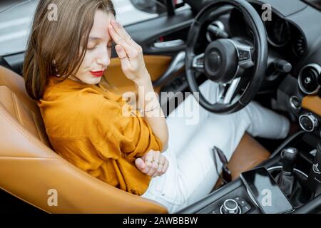 Young woman feeling stressed, having a headache while sitting on the driver's seat of convertible car Stock Photo
