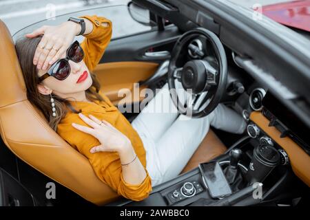 Young woman feeling headache while sitting on the driver's seat of convertible car. View from above Stock Photo