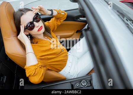 Young woman feeling headache while sitting on the driver's seat of convertible car. View from above Stock Photo