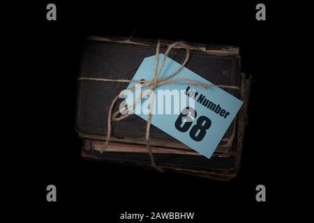 Antique old books stacked into a pile tied with string with auction house lot number on a blue tag label. Antiques auction concept Stock Photo