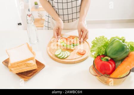 making sandwich with bread, cheese, salad and ham with hands on wooden cutting board Stock Photo