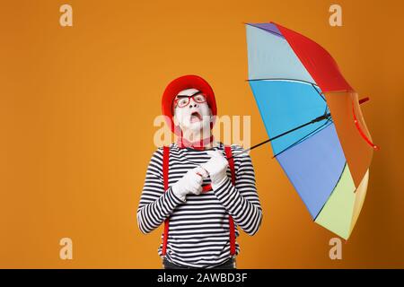 Mime looking up with multi-colored umbrella isolated on empty orange background in studio Stock Photo