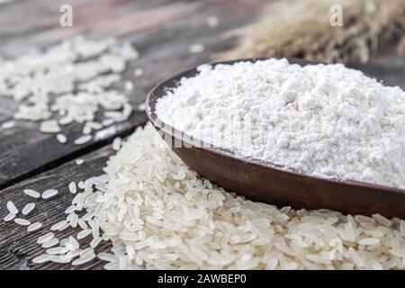 Rice flour in a bowl on a pile of white rice on old boards. Jasmine rice for cooking. Stock Photo