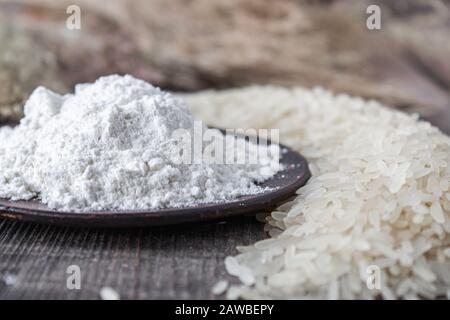 Rice flour in a bowl near the heap of white rice on old boards. Jasmine rice for cooking. Close-up. Stock Photo