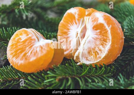 Ripe peeled slices of tangerine without peel lie on the green branches of a Christmas tree. Citrus fruits, tangerines or oranges. Close-up. Stock Photo