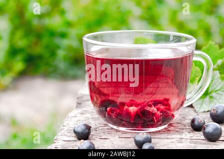 Glass cup of fruit tea with black currant berries on a wooden table in the open air. Close-up. Stock Photo