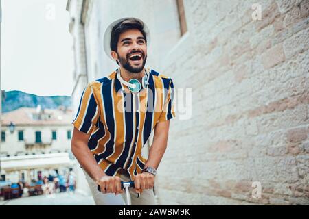 Joyful handsome man riding a scooter, having fun. Selective focus. Stock Photo